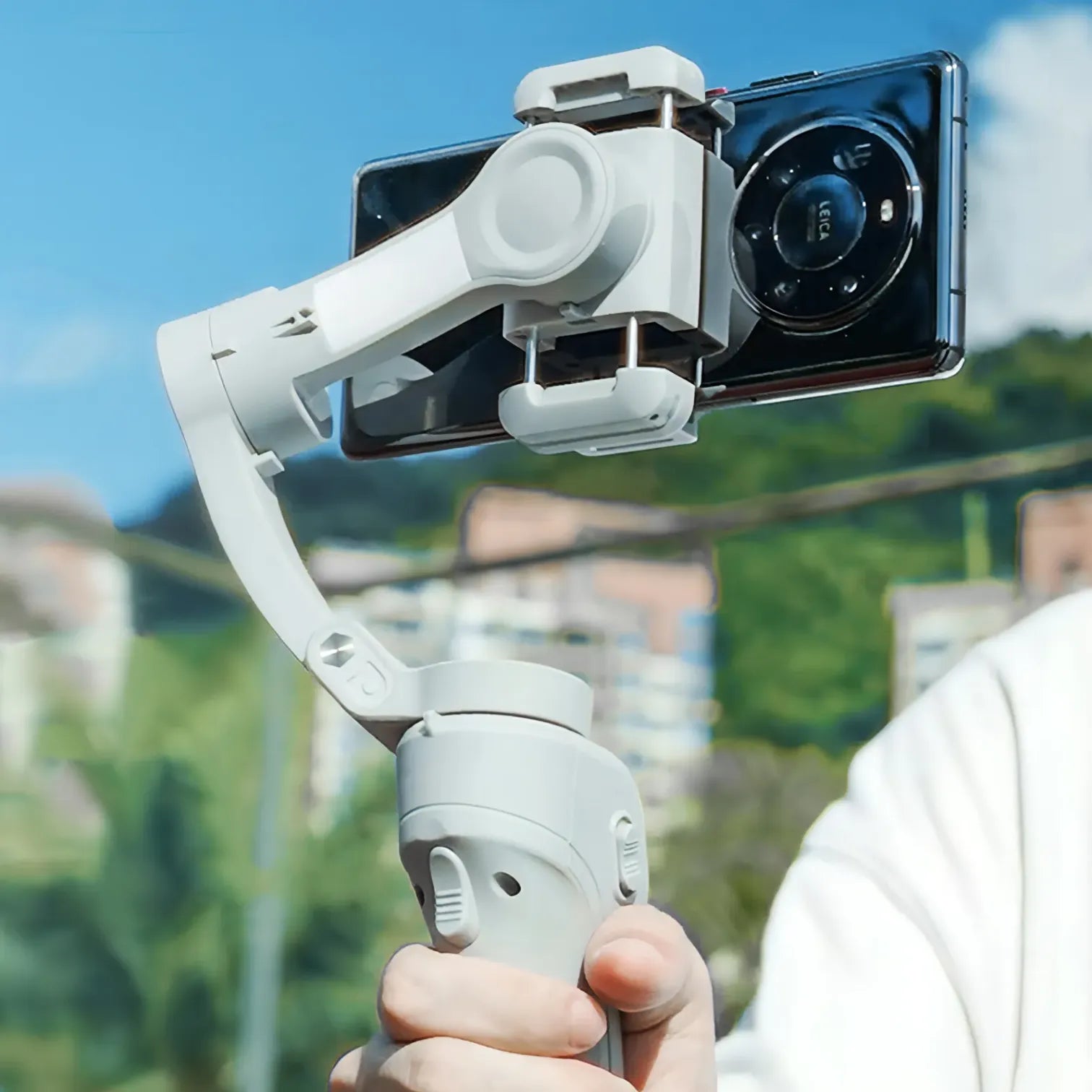 Hand hält einen Danxon Gimbal mit Smartphone vor klarem Himmel und unscharfem Hintergrund